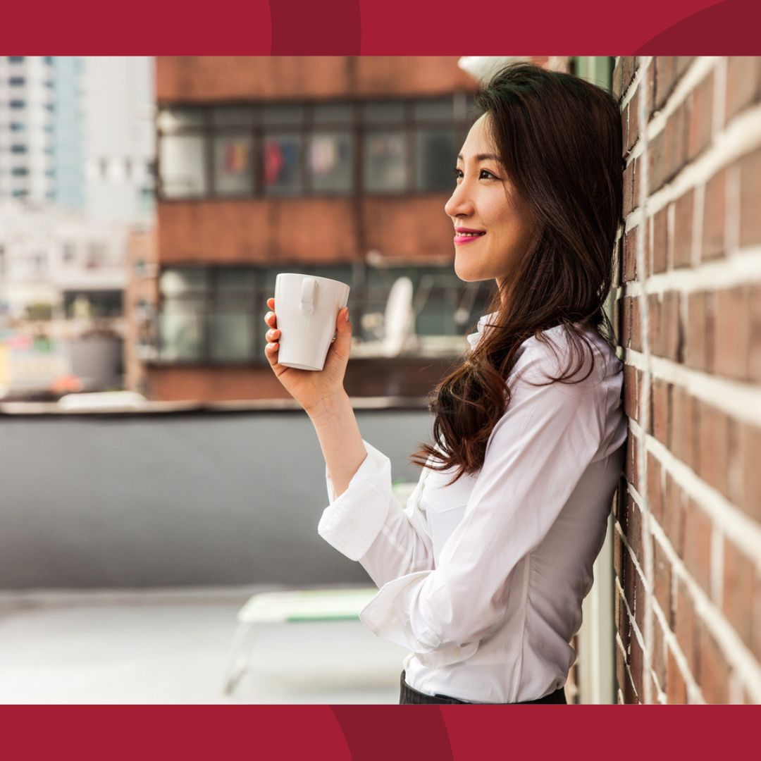 A woman leaning against a brick wall and holding a coffee mug.